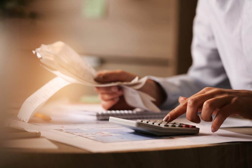 Person using a calculator while going through bills to create and stick to a budget.