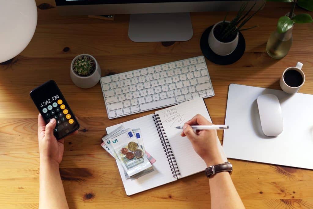 Close-up of an entrepreneur working from home, calculating savings and finances, reflecting on passive income ideas that don’t require tech skills, with money and notes visible.